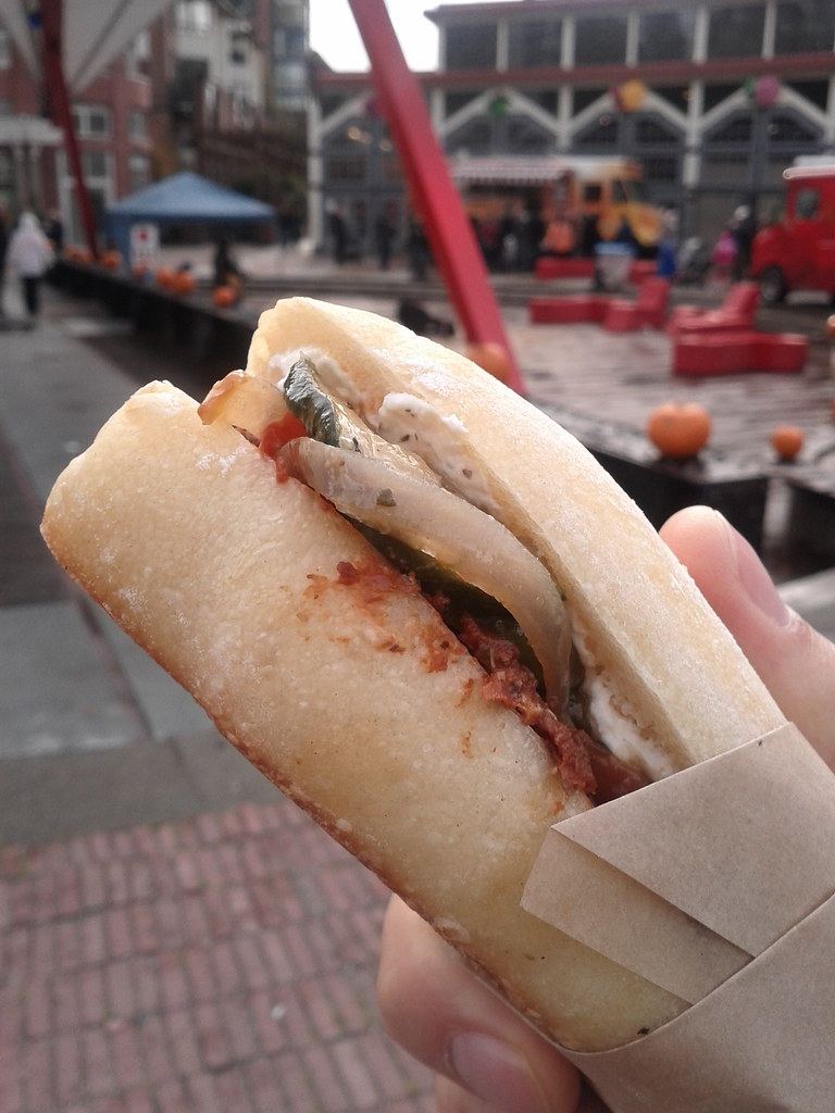 A hand holding a sandwich at an outdoor food stall